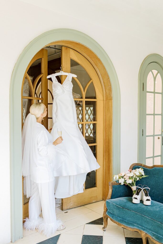 bride admiring wedding gown hanging in door frame